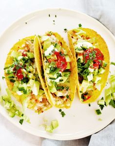 two tacos are sitting on a plate with avocado and tomato toppings