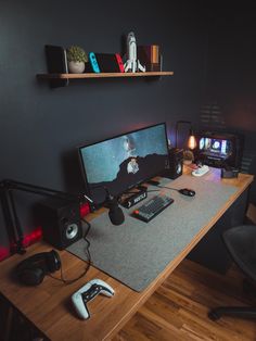 a desk with a computer, keyboard and two controllers on it in front of a black wall