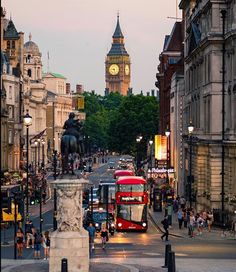 a busy city street with double decker buses and people walking on the sidewalk near big ben