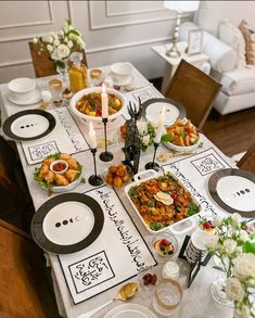 a table set with plates and bowls filled with food, candles and flowers on it