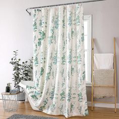 a white shower curtain with green leaves on it in a bathroom next to a window