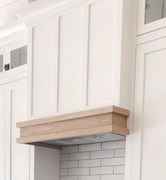 a kitchen with white cabinets and wood trimmings on the hood over the stove