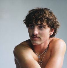 a man with curly hair and no shirt is posing for the camera while wearing a chain around his neck