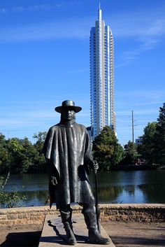 a statue of a man wearing a hat and holding a cane in front of a body of water