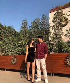 a man and woman standing next to each other in front of a fence with trees