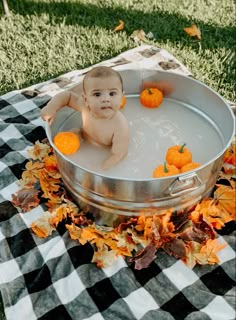 a baby sitting in a metal pan filled with water and oranges on a black and white checkered blanket