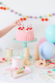 a table topped with a pink cake and lots of balloons next to a white wall