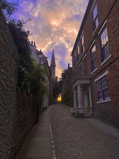 a cobblestone street lined with brick buildings under a cloudy blue and pink sky