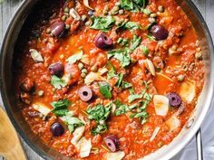 a pan filled with meat and olives on top of a wooden table