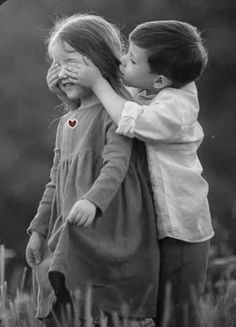 two children hugging each other in the middle of a field with a red heart on it