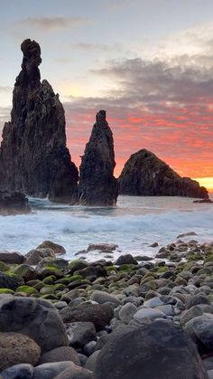 the sun is setting over some rocks on the beach with waves crashing in to shore