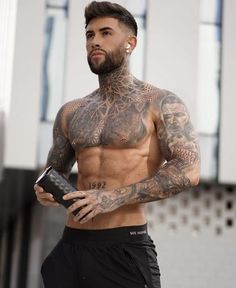 a shirtless man with tattoos holding a book