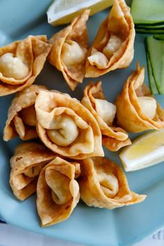 some dumplings are on a blue plate with cucumbers and lemon wedges