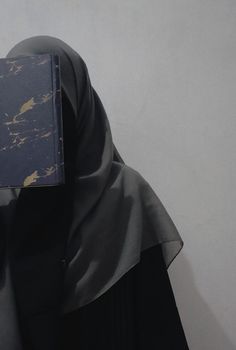 a woman wearing a black hijab with a blue book covering her face and head