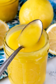 a spoon in a jar filled with lemon curd next to sliced lemons on a blue and white cloth