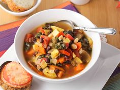 a white bowl filled with soup next to a piece of bread on top of a table