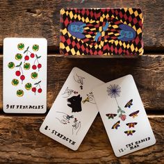 three playing cards sitting on top of a wooden table next to a box with stickers