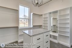 an empty walk in closet with white cabinets and granite counter tops, along with a chandelier hanging from the ceiling