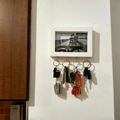 a bunch of keys hanging on a wall with a picture frame above it and some other key holders attached to the wall