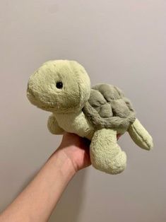 a hand holding a small stuffed turtle in it's left arm and the top part of its body