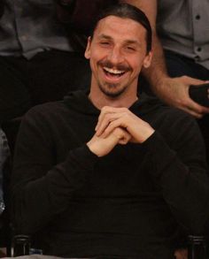 a smiling man sitting in the stands at a basketball game