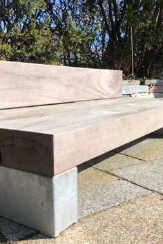 a wooden bench sitting on top of a cement slab next to some grass and trees