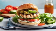 a grilled chicken sandwich with lettuce, tomatoes and cucumbers on a plate