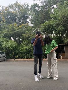 two people standing in the middle of a parking lot taking pictures with their cell phones