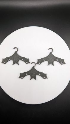 two black metal leaves on a white circular plate with hooks in the shape of an occupant