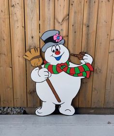 a snowman with a hat and scarf holding a broom in front of a wooden fence