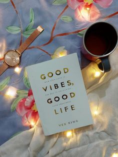 a cup of coffee sitting on top of a bed next to a book with the words good vibes, good life