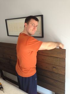 a man in an orange shirt leaning on a bed with his arm over the headboard