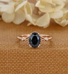 a black diamond ring sitting on top of a wooden table next to white flower petals