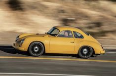 an old yellow car driving down the road