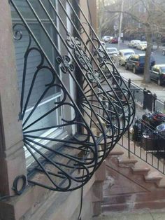 an iron stair rail on the side of a building with cars parked in the street behind it