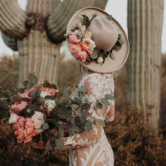 a woman in a dress and hat with flowers on her head standing next to cacti