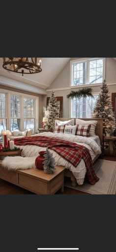 a bedroom decorated for christmas with red and white plaid blankets on the bed, trees in the window