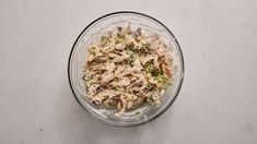 a glass bowl filled with chicken salad on top of a white countertop next to a wooden spoon