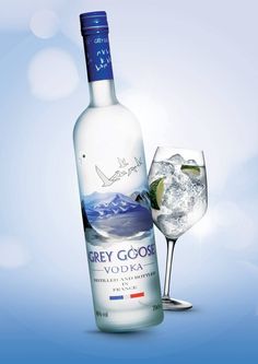 a bottle of grey goose vodka next to a glass filled with ice and garnish