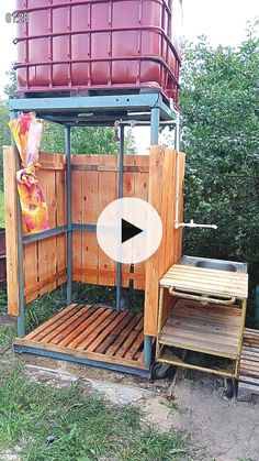 an outdoor shower made out of wooden pallets and metal frame with a red bucket on top