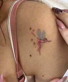 a small tattoo on the back of a woman's shoulder, with a pink ribbon around it