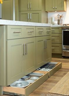 an open drawer in the middle of a kitchen with green cabinets and stainless steel appliances