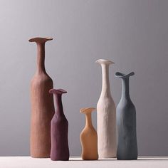 four different colored vases sitting on top of a table next to eachother