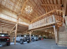 two jeeps are parked in a large garage with wooden walls and beams on the ceiling