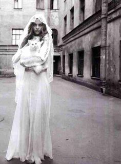 a woman in a wedding dress holding a cat and posing for a photo with an old building behind her