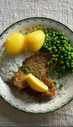 a white plate topped with fried fish, peas and lemons