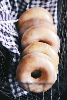 four glazed donuts in a wire basket on a checkered cloth covered tablecloth