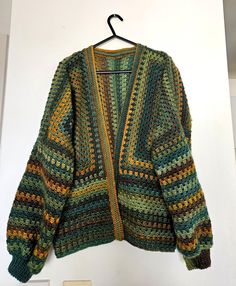 a crocheted sweater hanging up on a white wall next to a coat hanger