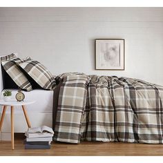 a bed with plaid sheets and pillows on top of it next to a night stand