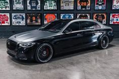 a black car parked in front of a wall full of license plates and numbers on it